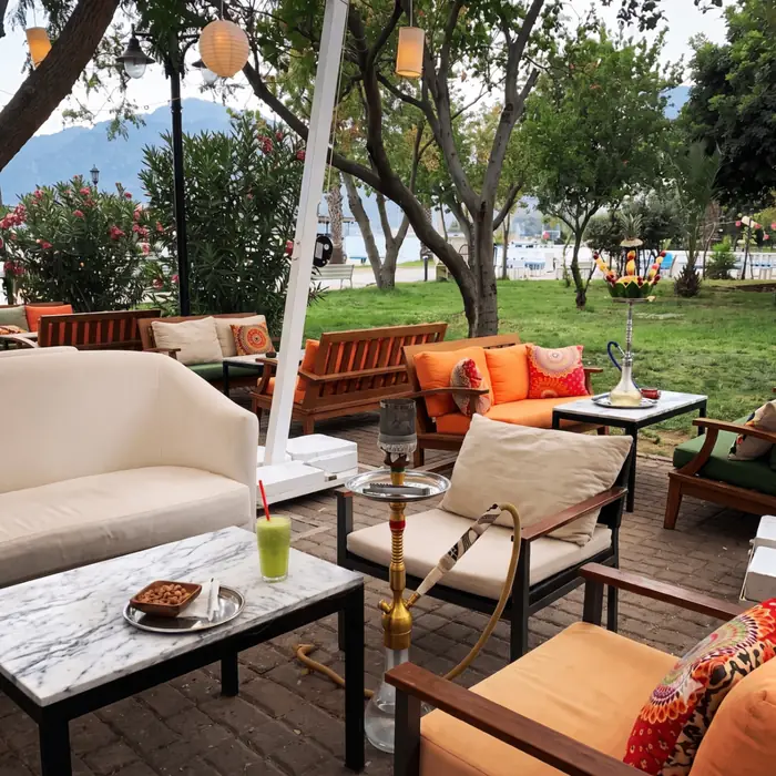 Marmara masalar, turuncu yastıklı bahçe koltukları ve marina manzarası